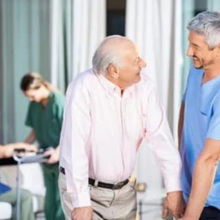 An elderly man receiving assistance from a healthcare worker in a hospital setting.