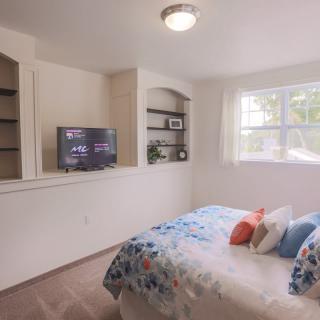 A cozy bedroom with built-in shelves, a television, and a bed adorned with colorful pillows.