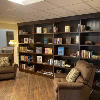 A cozy reading area featuring bookshelves filled with various books, accompanied by comfortable armchairs and a wooden floor.