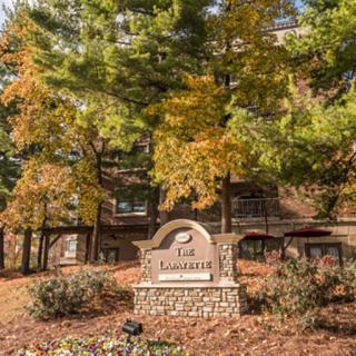 A scenic view of a building surrounded by autumn trees with a prominent stone sign in the foreground.