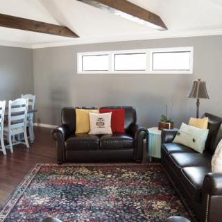 A cozy living room with leather sofas, a colorful rug, and wooden beams overhead.