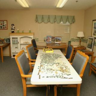 A room with a large table and chairs, featuring an incomplete puzzle spread across the surface.