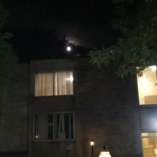 A serene night scene featuring the moon peeking through the clouds above a building.