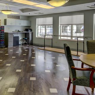 A well-lit room with multiple chairs and tables, featuring large windows and wooden flooring.