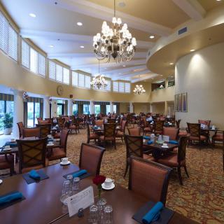 A spacious and elegant dining area featuring chandeliers, numerous tables, and comfortable seating.