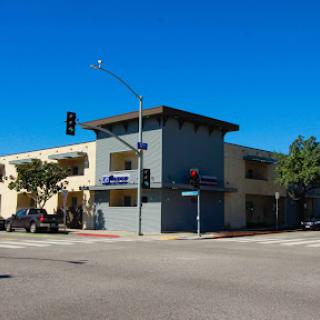 A modern commercial building at a street intersection under a clear blue sky.