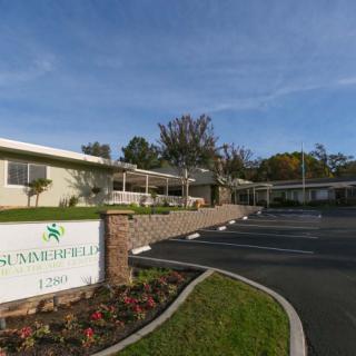 A building with a sign in front, adjacent to a parking lot and surrounded by landscaped greenery.