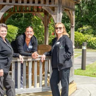 Three people standing and leaning on a gazebo in a sunny outdoor setting.