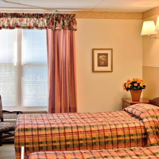 A cozy bedroom with twin beds, adorned with plaid bedding and soft pink curtains.