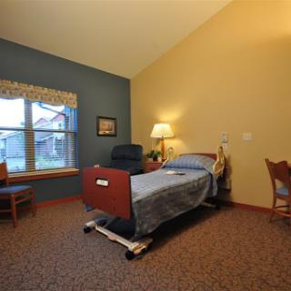 A cozy hospital room featuring a bed, chairs, and natural light from the window.