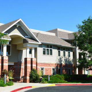 A suburban residential building with a mix of brick and siding, surrounded by trees under a clear blue sky.