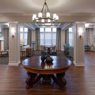 A spacious and elegantly decorated living room with a central wooden table and chandelier.
