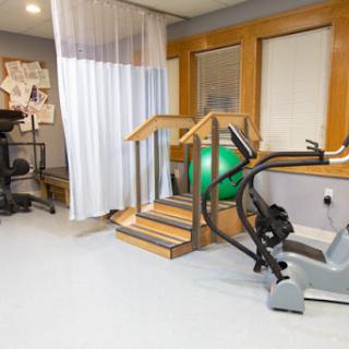 A well-equipped therapy room featuring a set of stairs for rehabilitation exercises, an exercise bike, and a green exercise ball.