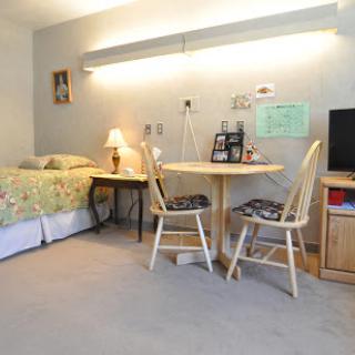 A cozy and well-lit bedroom featuring a bed, a small dining area with chairs and a table, and a television.