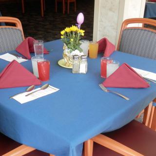 A neatly set dining table with red napkins, drinks, and a floral centerpiece.