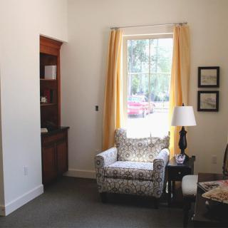 A cozy living room corner with an armchair by the window, complemented by yellow curtains and a lamp.