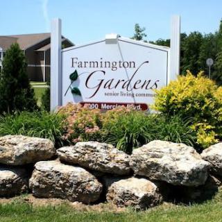A welcoming entrance sign for Farmington Gardens, surrounded by rocks and lush greenery.