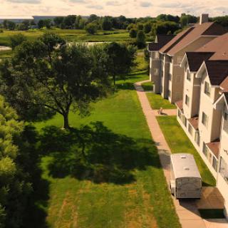 A serene residential area featuring green lawns, a large tree, and a parked trailer next to the buildings.