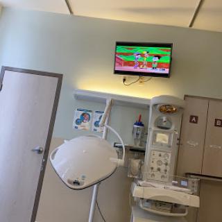 A view of a hospital treatment room with medical equipment and a TV displaying a cartoon.