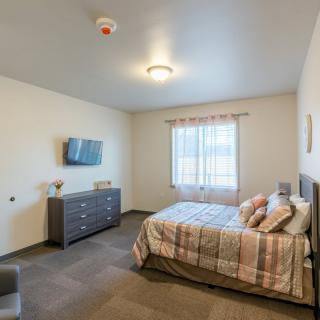 A modern bedroom with a neatly made bed, wall-mounted television, and dresser.