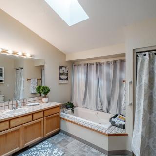 A spacious bathroom features a large bathtub, a vanity with dual sinks, and a skylight that brightens the space.
