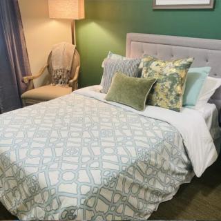 A cozy bedroom setup with a neatly made bed, featuring patterned bedding and decorative pillows, complemented by a nearby chair and lamp.