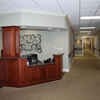 A modern office reception area featuring a wooden desk and decorative artwork, leading to a long hallway.