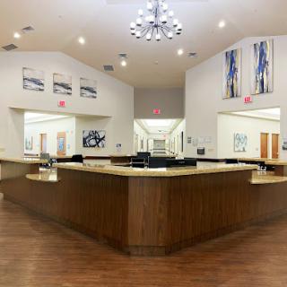 A spacious and modern reception area featuring a wooden counter, elegant chandelier, and contemporary artwork.