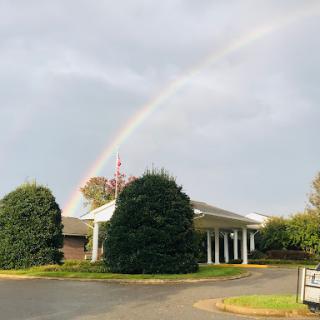 A beautiful rainbow appears above a serene building on a cloudy day.