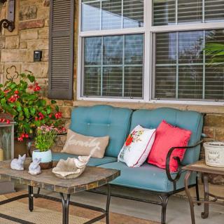 A cozy patio setup with a sofa, colorful cushions, and potted plants.