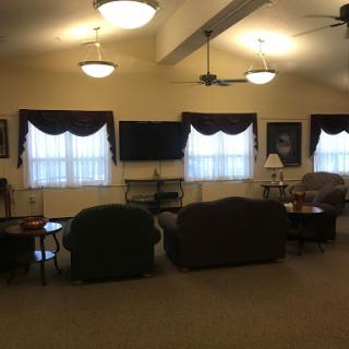 A cozy lounge area with sofas, natural light from large windows, and ceiling fans for comfort.