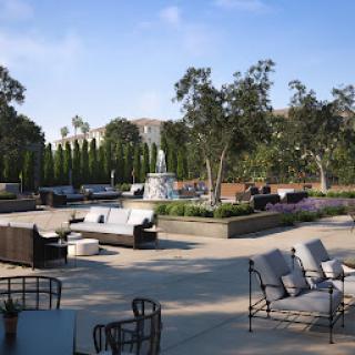 A serene outdoor lounge area featuring comfortable seating and a tranquil water fountain, surrounded by lush greenery.