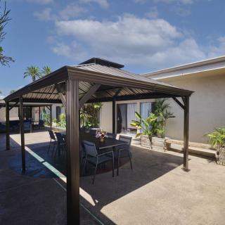 A sunny patio with a pergola and outdoor furniture surrounded by plants.