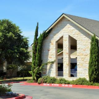 A charming stone building surrounded by greenery and a well-maintained parking area.