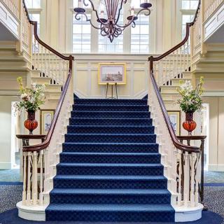 A grand staircase with a blue carpet and elegant chandelier in an opulent interior.