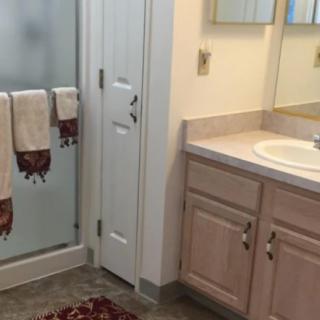 A bathroom featuring a sink with a mirror, towels hanging near a shower, and a rug on the floor.
