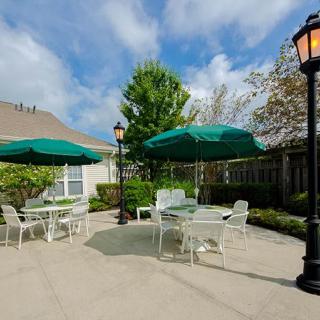 Outdoor patio area with tables, chairs, and green umbrellas under a blue sky.