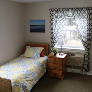 A simple and cozy bedroom with a single bed, nightstand, and a window adorned with patterned curtains.