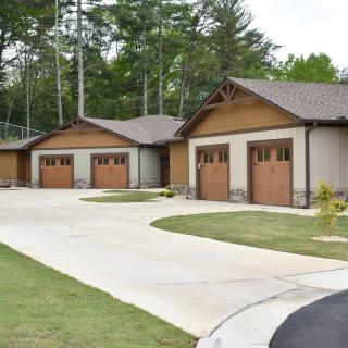 Row of garages with wooden doors in a residential area surrounded by trees.