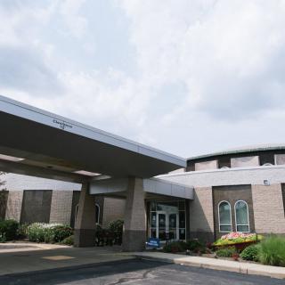 A modern building with a covered entrance and a parking area under a cloudy sky.