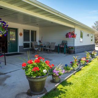 A sunny patio with outdoor seating, surrounded by colorful potted plants and hanging flower baskets.