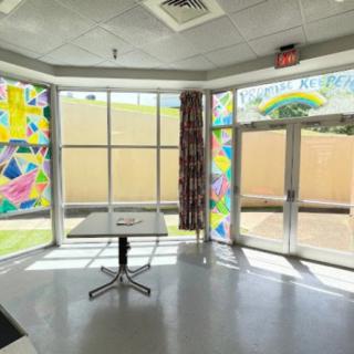 A brightly lit room with colorful decorations on the windows, featuring a central table and ceiling lights.