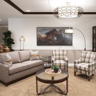 A cozy living room with a sofa, two plaid armchairs, a round coffee table, and decorative artwork on the wall.