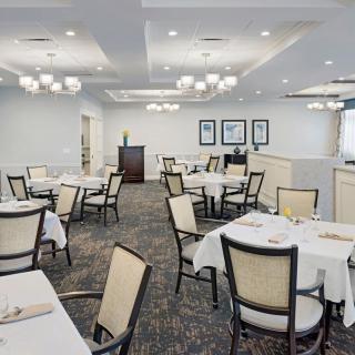 An elegant and empty dining room with neatly arranged tables covered in white tablecloths.