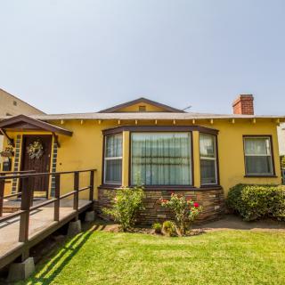 A yellow bungalow with a front lawn and ramp, featuring large windows and a small garden.