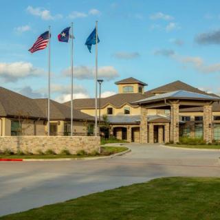 A well-maintained building with a driveway, adorned with three flags waving against a partly cloudy sky.