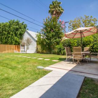 A sunny backyard with a lawn, patio furniture, and an umbrella.
