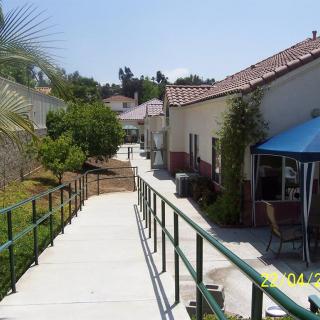 A concrete pathway with a metal railing runs alongside buildings and gardens under a clear sky.