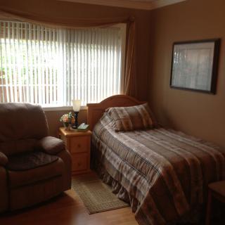 A cozy bedroom with a single bed, armchair, and window allowing natural light to fill the space.