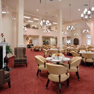 A spacious dining area featuring elegant chandeliers, comfortable seating, and a warmly carpeted floor.